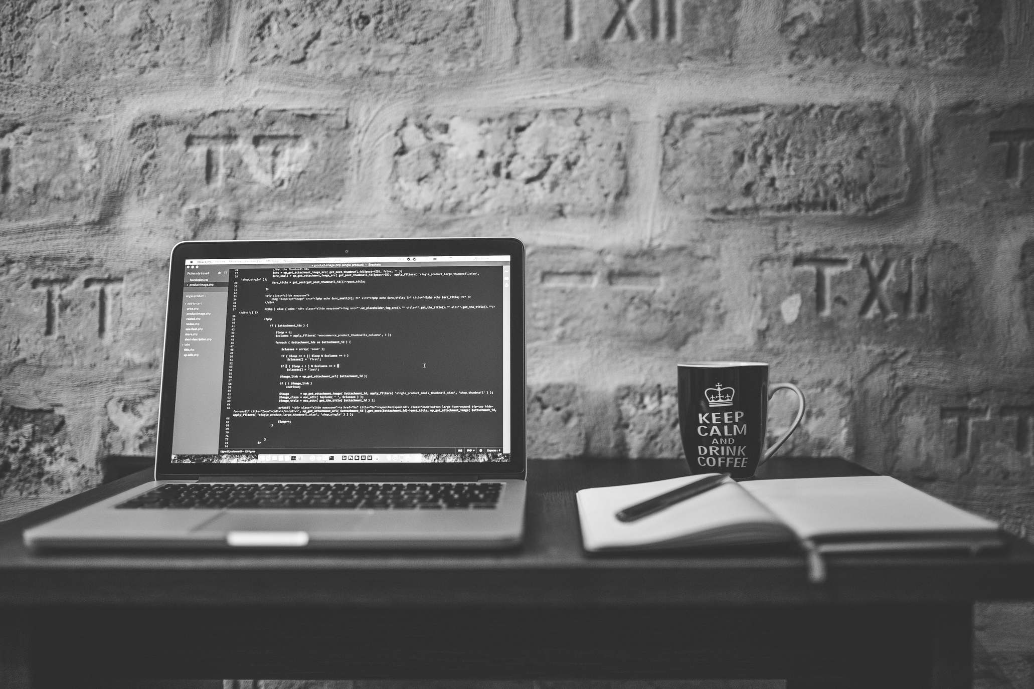 Wide view of a coding workspace with a laptop, mug, and notebook.